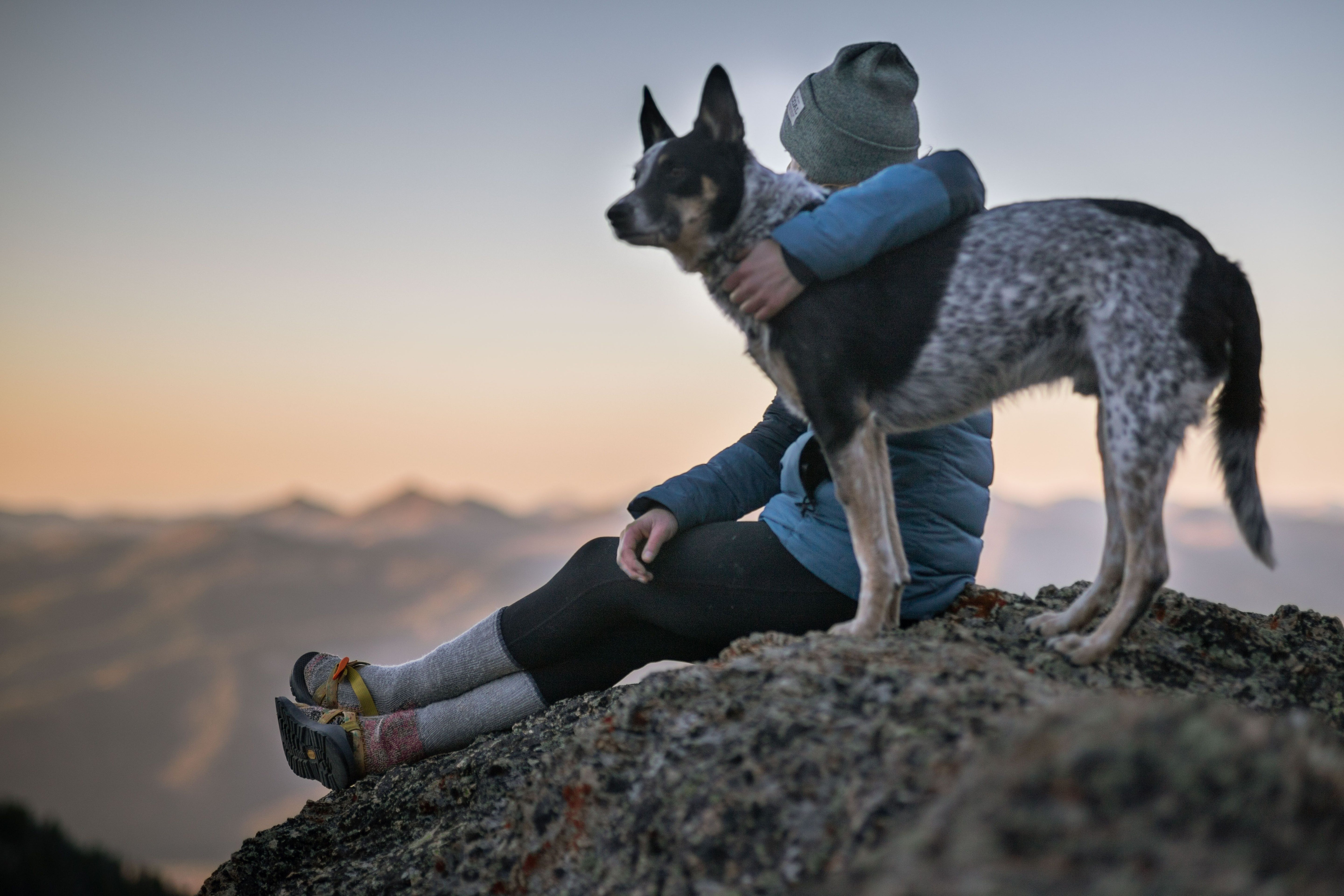 Hiker sitting on a rocky mountain summit at sunrise beside an attentive dog on a leash
