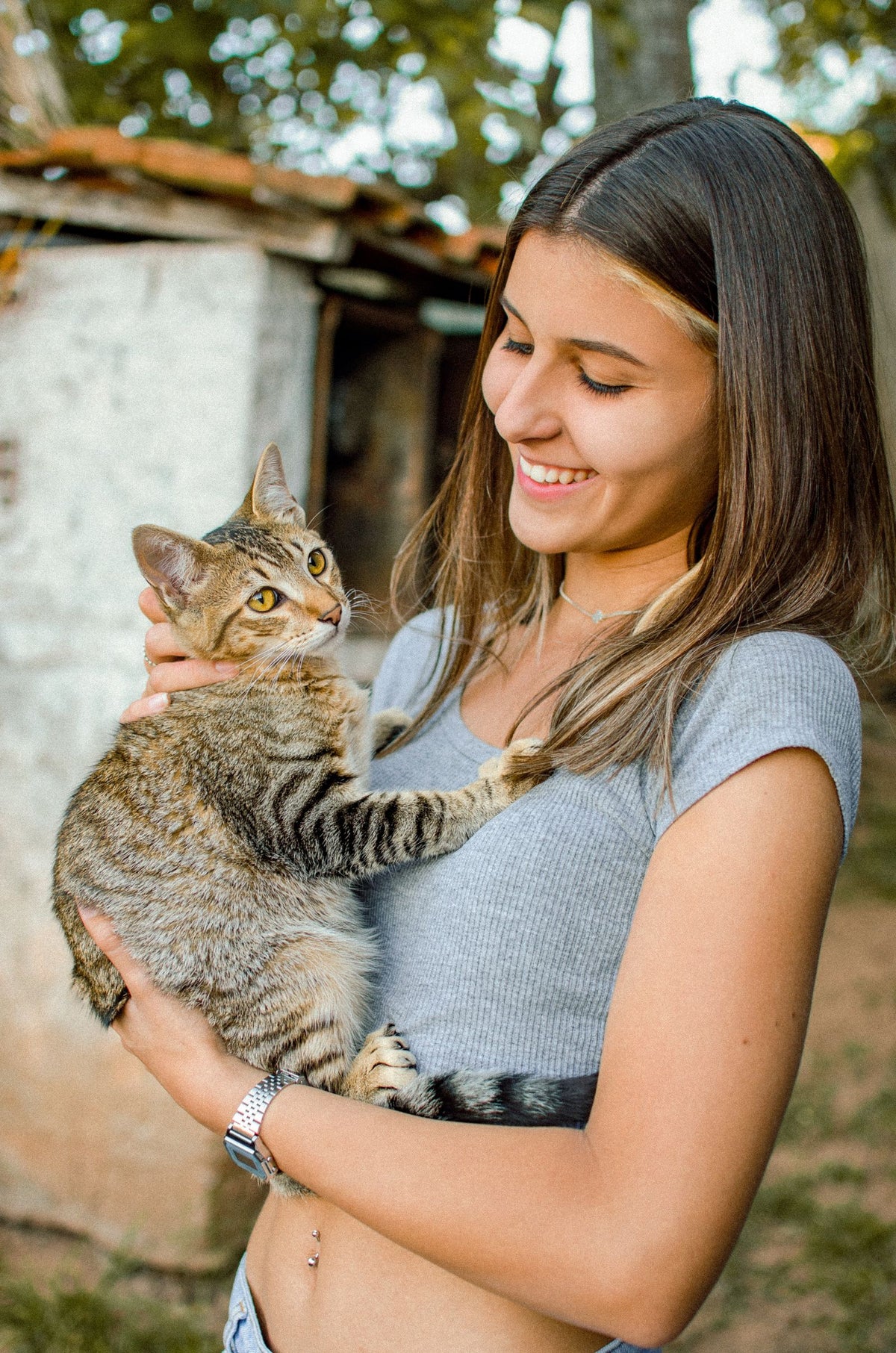 A smiling woman holding a tabby cat in her arms outdoors