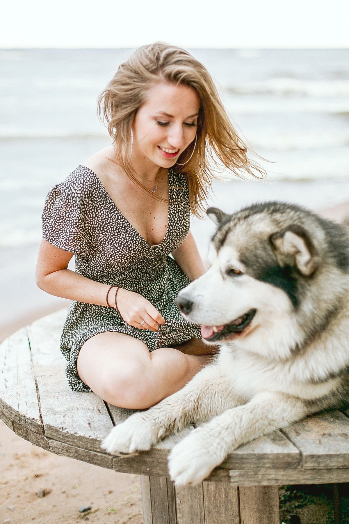 A woman sitting outdoors beside a large husky dog resting calmly next to her