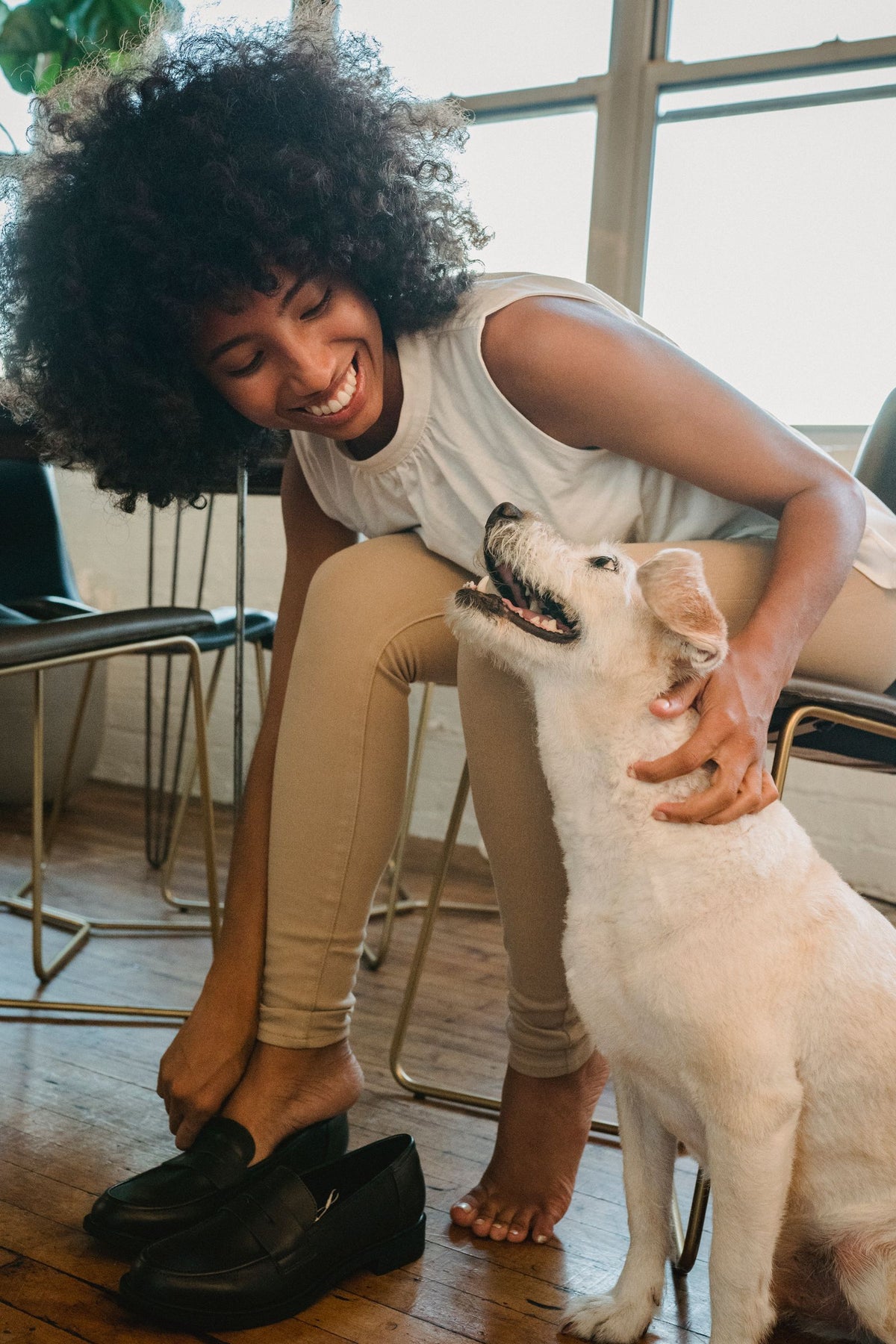 A woman sitting at home smiling as a cream-coated dog reaches up to her.